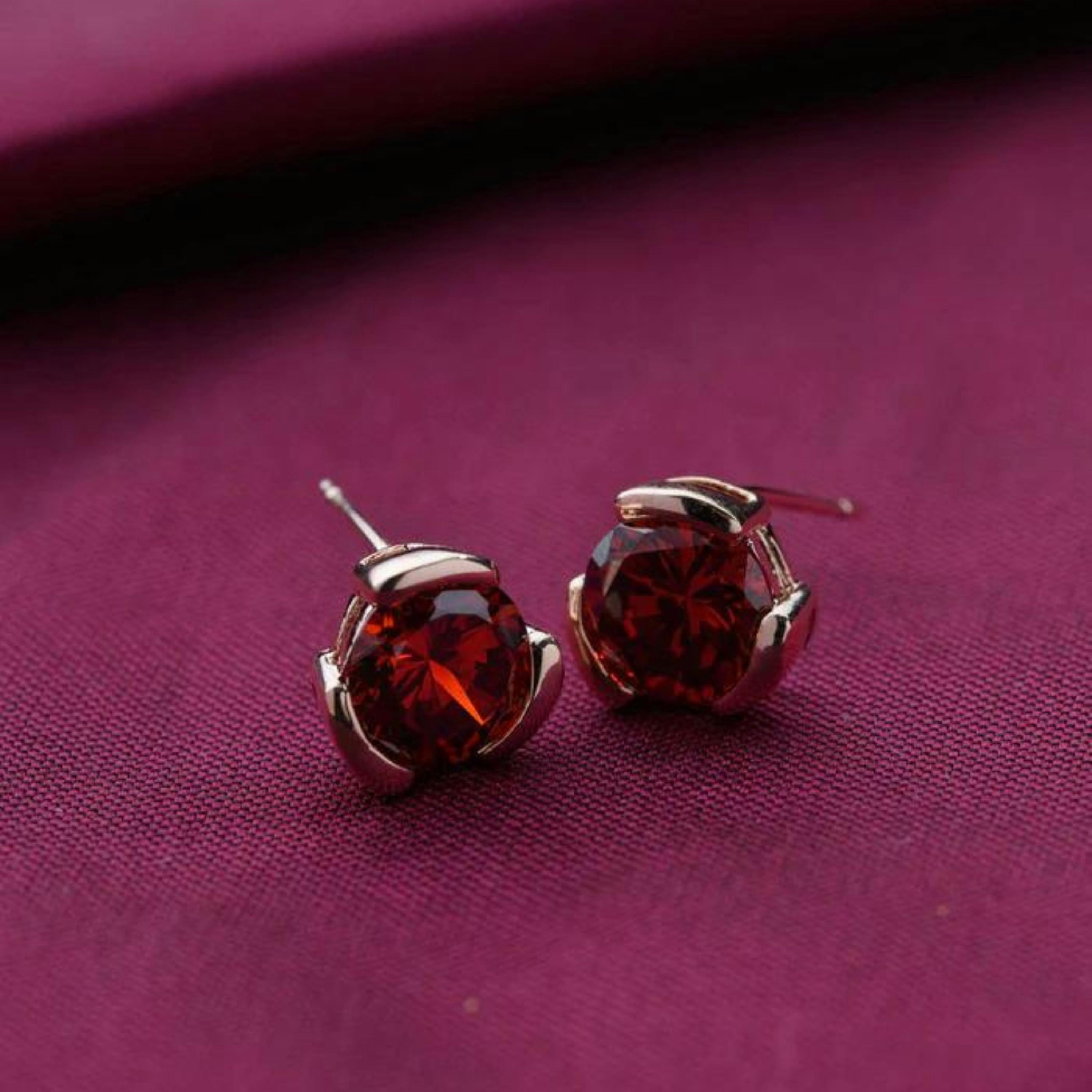 Close-up of elegant red jewel earrings on deep purple fabric background.