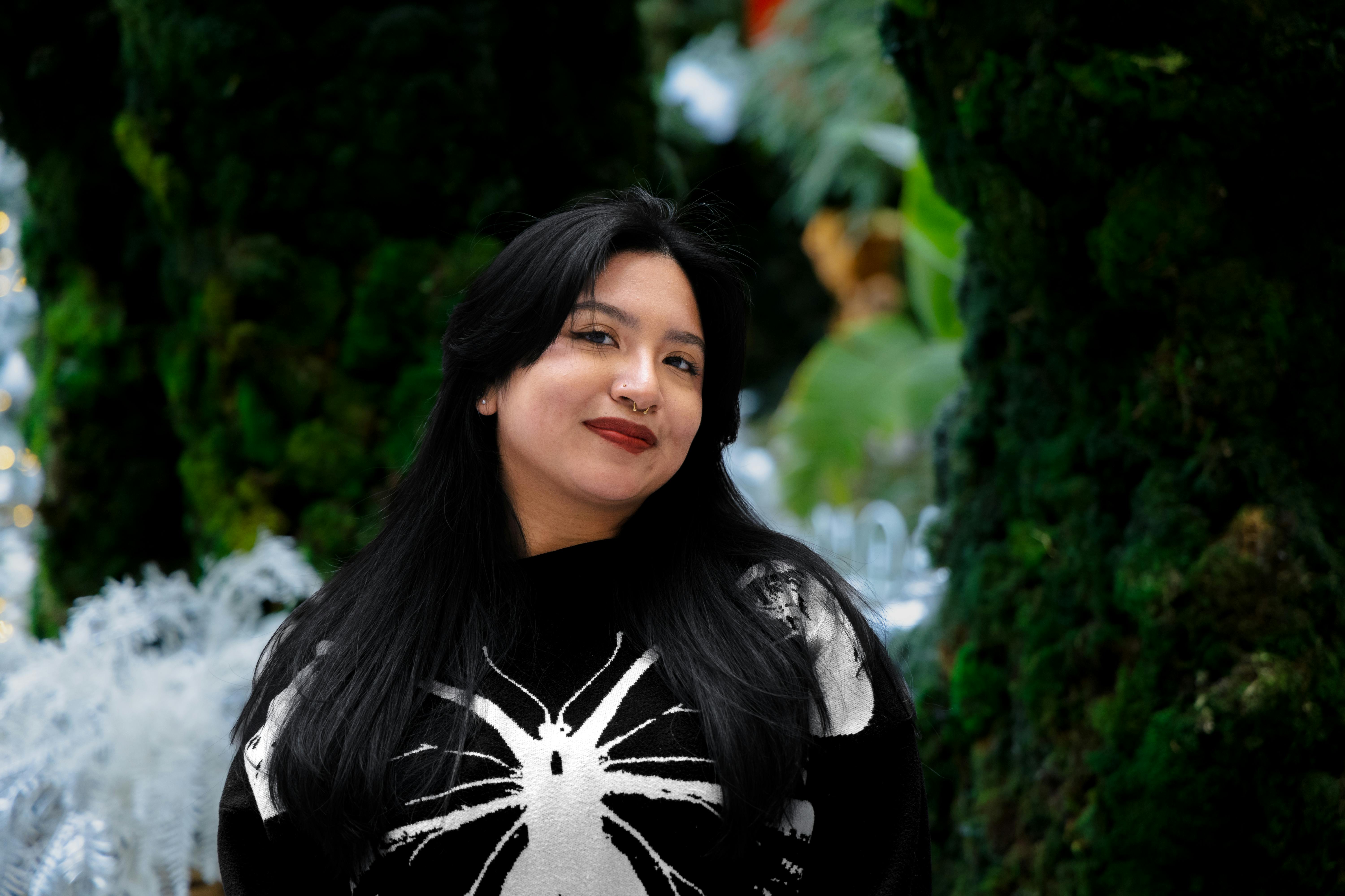 Confident woman posing outdoors near lush greenery.